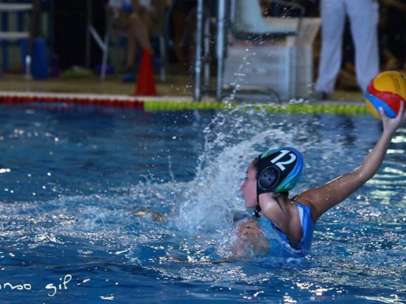 Joven jugando waterpolo en una piscina, lanzando el balón con fuerza.
