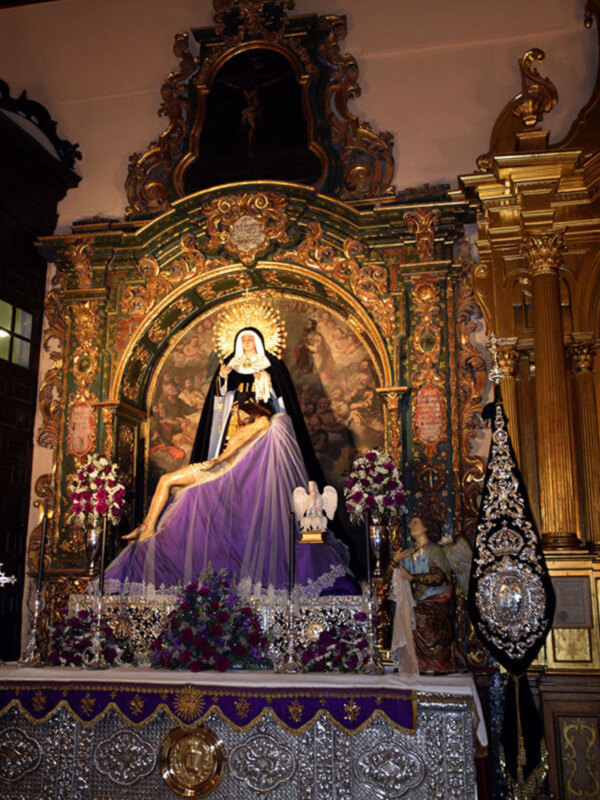 Altar con imagen de la Virgen de la Soledad, adornado con flores y ornamentos dorados.
