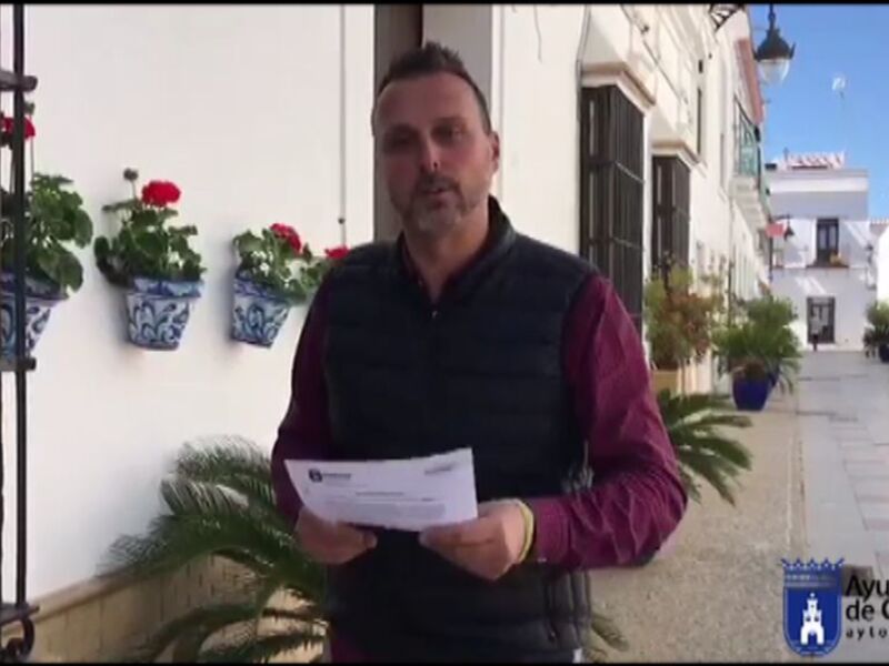 Persona con documentación en la mano, en una calle típica de Chipiona, España, con fachadas blancas y detalles florales.