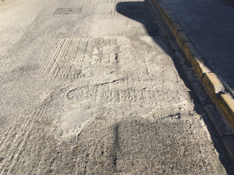 Pavimento de asfalto con bordillo y sombras de edificios.