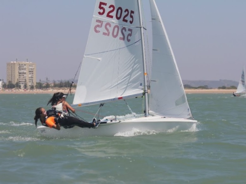 Competencia de vela en el mar, barco con número 52025 navegando con una persona en el remo y otra en el timón.