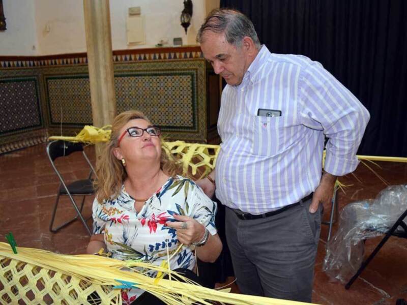 Una mujer y un hombre trabajan juntos en la elaboración de una cesta de mimbre en un ambiente decorado con azulejos.