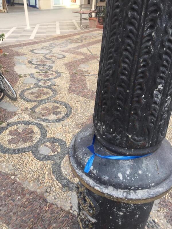 Detalle de una columna con mosaico de piedras y un poste de metal en un patio exterior.