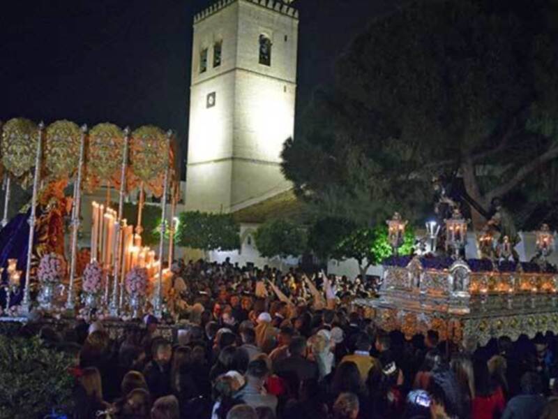 Procesión nocturna con estandartes y pasos de Jesús en una plaza iluminada.
