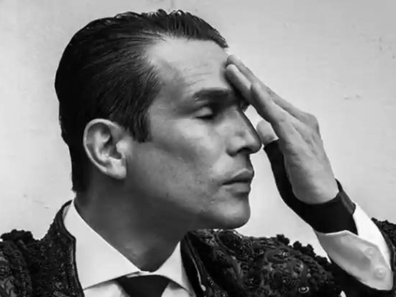 Retrato en blanco y negro de un hombre con traje de flamenca, posando con una mano en el frente.