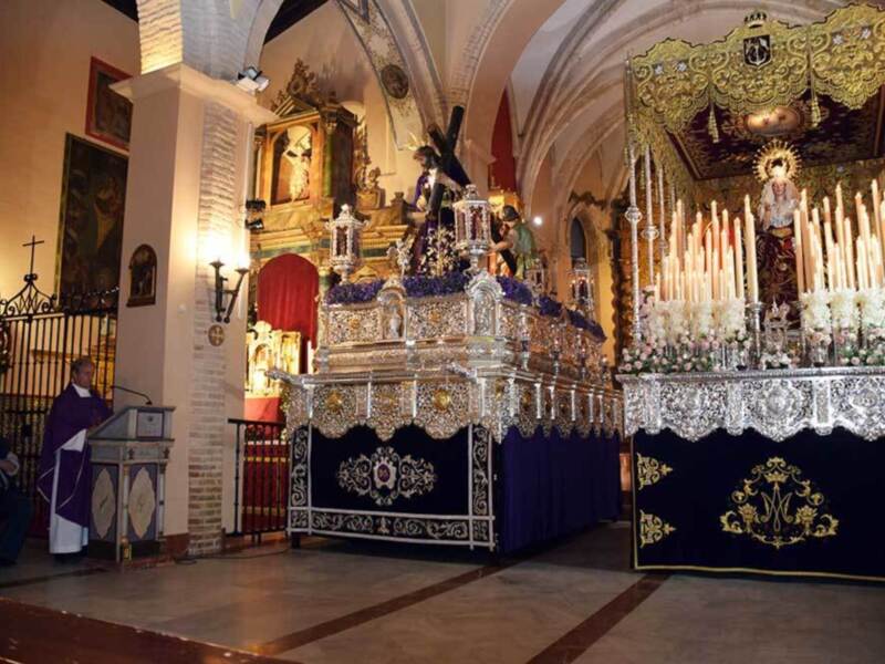 Procesión religiosa en una iglesia con estandartes y altares ornamentales, destacando la imagen del Cristo de la Buena Muerte y la Virgen de la Soledad.