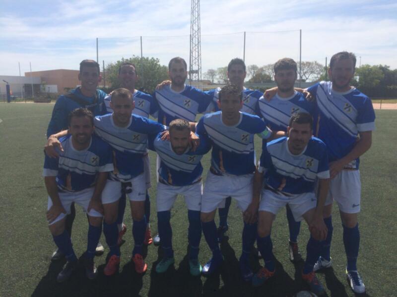Equipo de fútbol en campo de césped, con uniformes azules y blancos, posando para una foto en el centro del campo.
