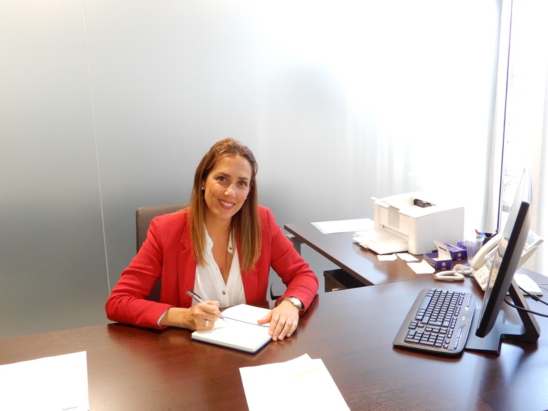 Profesional en su entorno de trabajo, sentada en su escritorio con equipo de oficina alrededor.