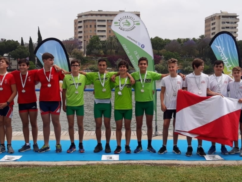 Equipo de remo infantil celebrando en el podio con medallas y bandera.