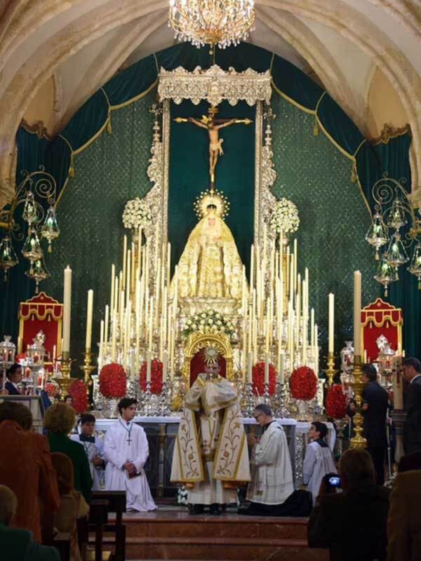 Interior de una iglesia con altares adornados, adornos florales y una imagen de la Virgen María en el centro.
