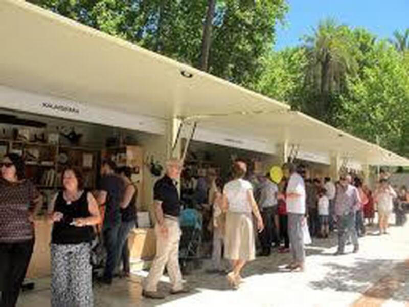 Feria de libros al aire libre con personas visitando puestos bajo toldos blancos.