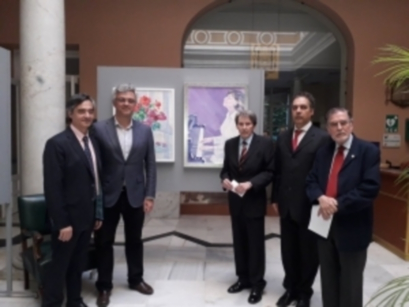 Grupo de hombres en trajes posando frente a una exposición de arte en un espacio interior clásico.