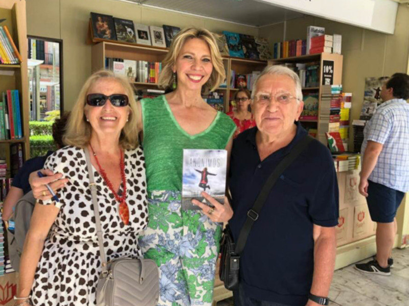 Una mujer sostiene un libro titulado 'Anónimos' mientras posa junto a dos personas en una librería.