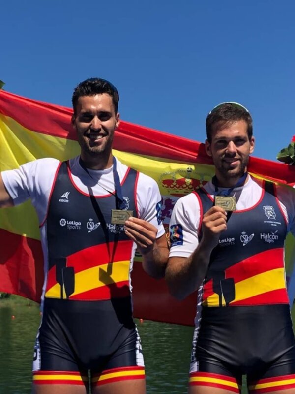 Campeones con bandera española y medallas en un evento deportivo al aire libre.