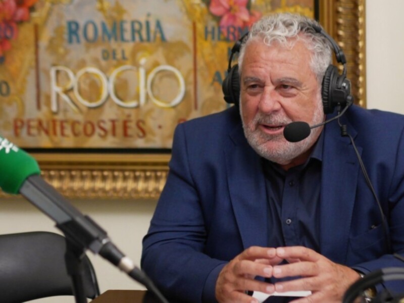 Entrevista en vivo con un invitado en un estudio de radio, fondo con cartel de 'Romería del Rocío'.