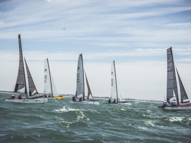 Competición de vela en el mar, con barcos navegando juntos bajo vientos fuertes.