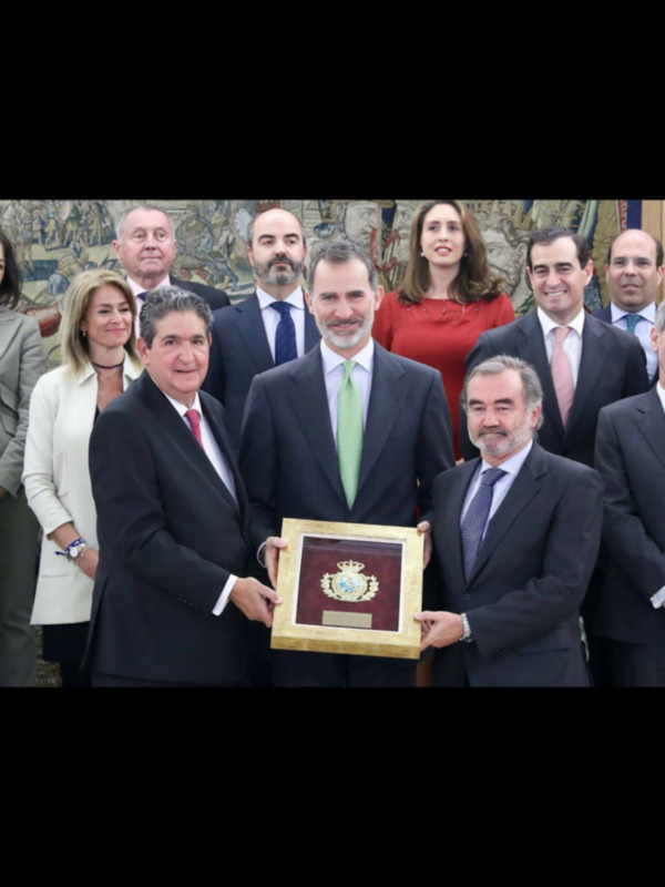 Un hombre sostiene una placa mientras sonríe, rodeado de otros individuos en una reunión formal.