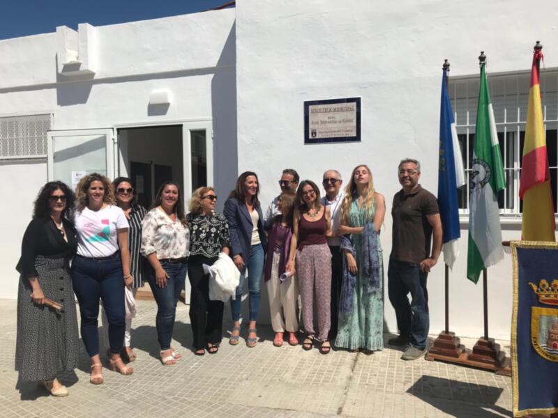 Grupo de personas posando frente a la Biblioteca Municipal de Chipiona, con banderas y placa de la institución.