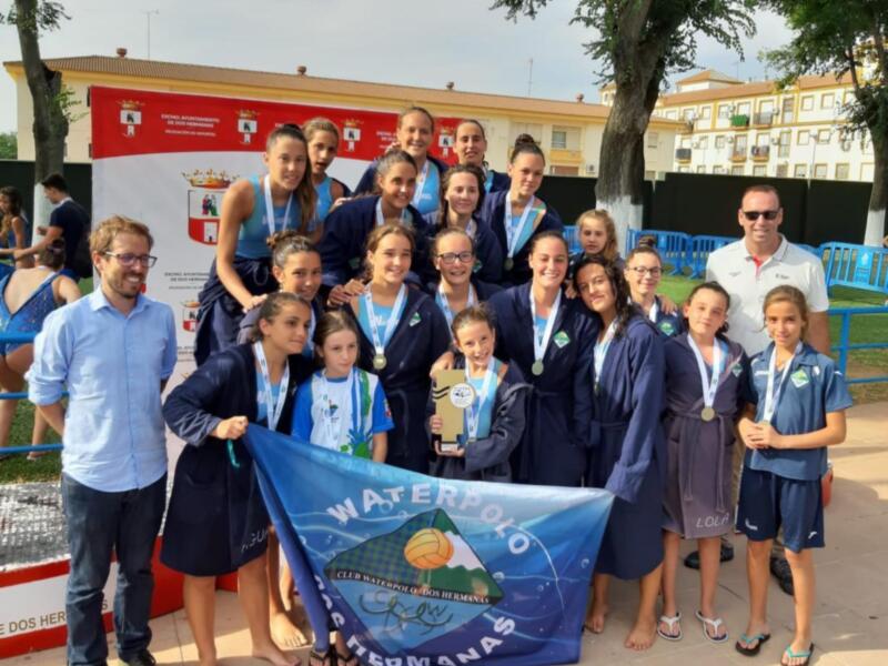Equipo de waterpolo celebrando con medallas y trofeo en un evento deportivo.