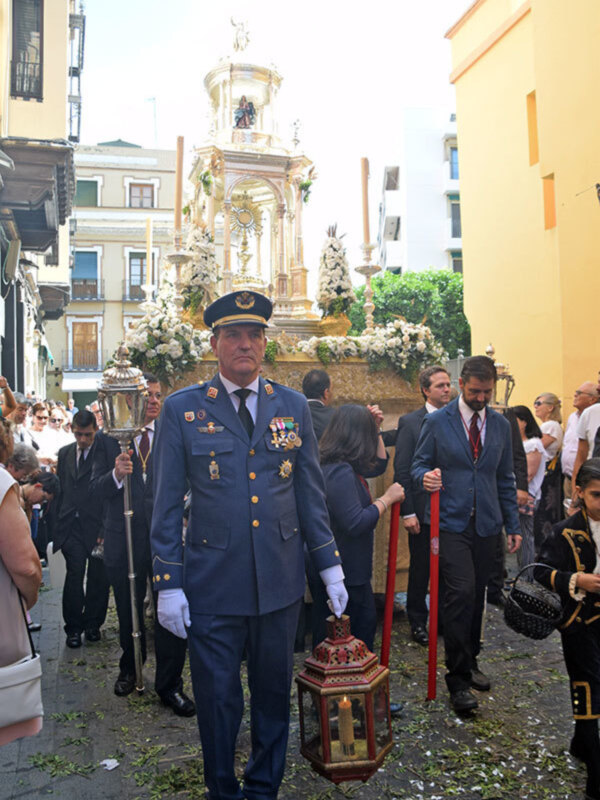 Un oficial de la Guardia Civil durante una procesión religiosa en una ciudad española, con un altar adornado y una multitud de espectadores observando el evento.