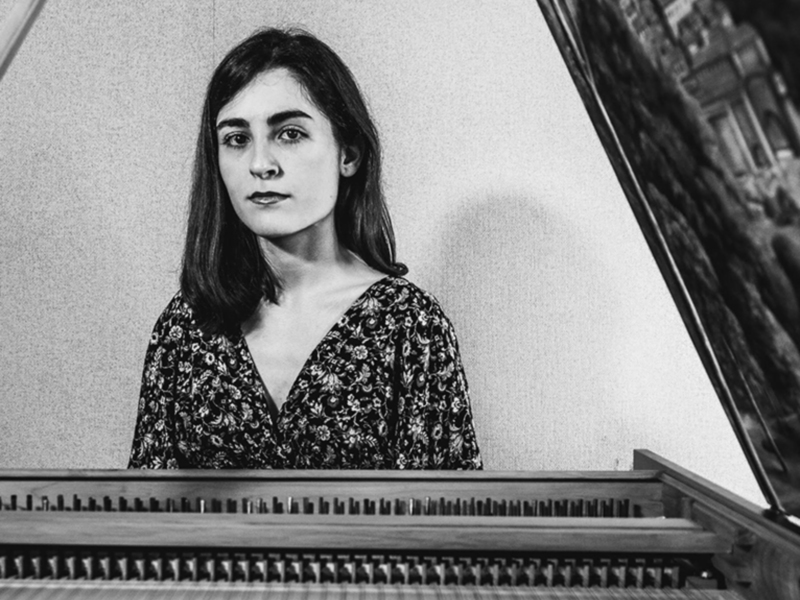 Retrato en blanco y negro de una mujer sentada frente a un piano clásico.