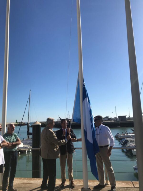 Oficiales levantando la bandera en un puerto marítimo bajo un cielo azul claro.