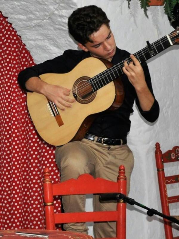 Joven tocando la guitarra clásica en un ambiente decorado con telas y muebles tradicionales.