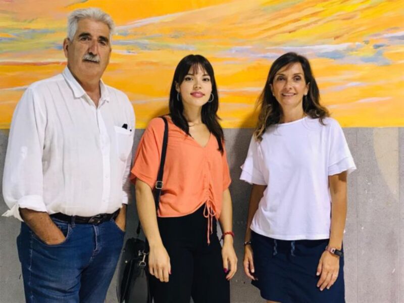 Tres personas posando juntas contra un fondo de arte abstracto en colores cálidos.
