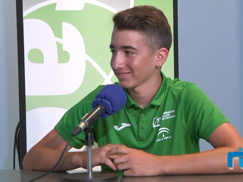 Joven hablando en un programa de radio con un micrófono y un logo en el fondo.