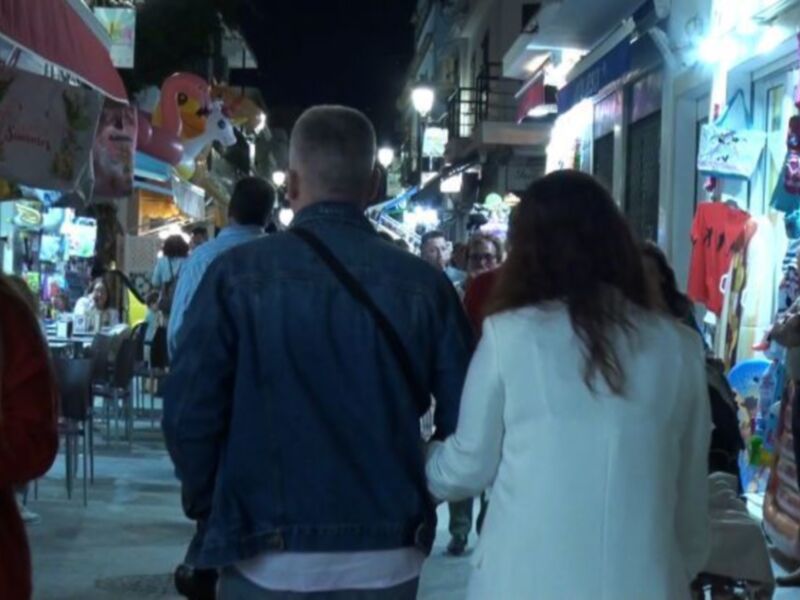 Calle animada de noche con tiendas y peatones caminando.