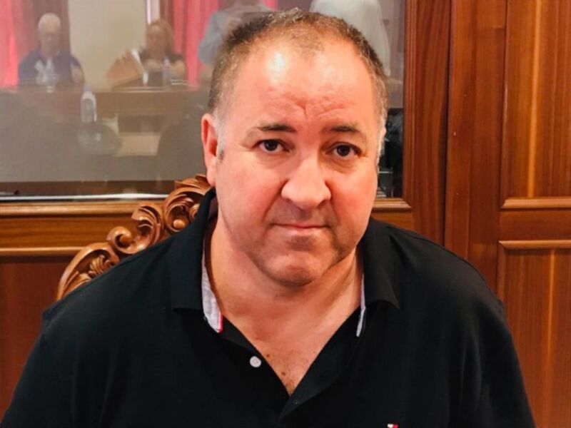 Persona en una reunión o sala de conferencias, vistiendo una camiseta negra y fondo de madera.