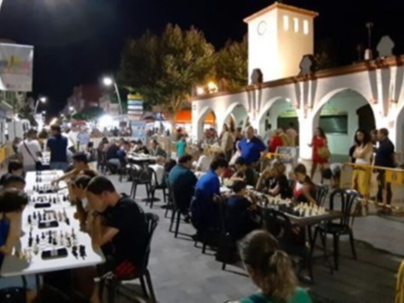 Jugadores de ajedrez participan en un torneo nocturno en una plaza animada y bien iluminada.