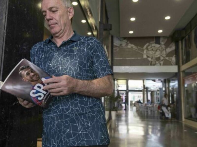 Un hombre en un centro comercial, sosteniendo un periódico con la imagen de un jugador de fútbol.