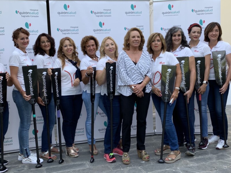 Equipo de voluntarios de Quirónsalud posando con palas de paddle surf en una actividad de promoción de salud.