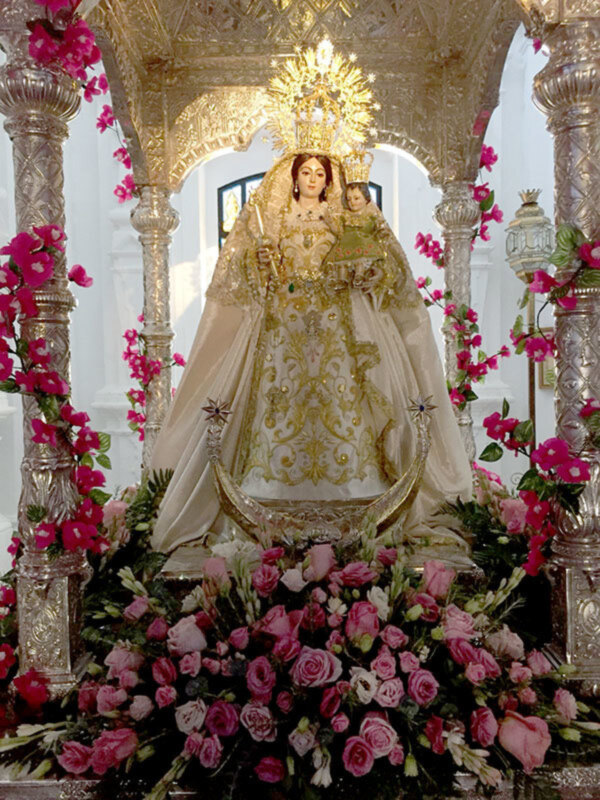Imagen de la Virgen María en un altar adornado con flores y decoración dorada.