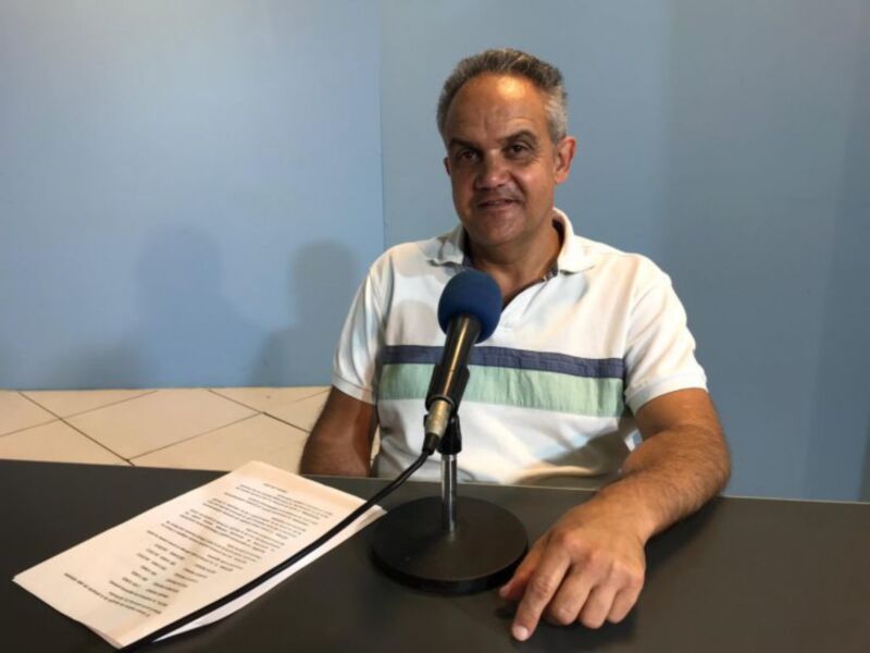 Hombre hablando en una entrevista o grabación de radio, con un micrófono y un documento en la mesa.