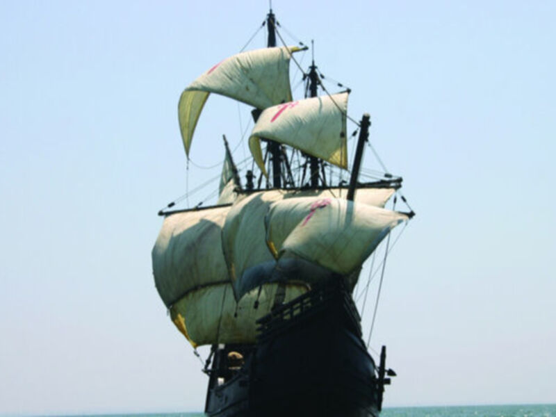 Imponente barco de vela con velas desplegadas en el horizonte, bajo un cielo azul claro.