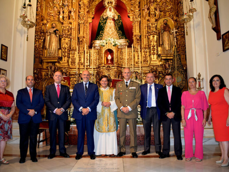 Gente posando en una iglesia frente a una imagen religiosa, con vestimentas formales y una decoración dorada en el fondo.