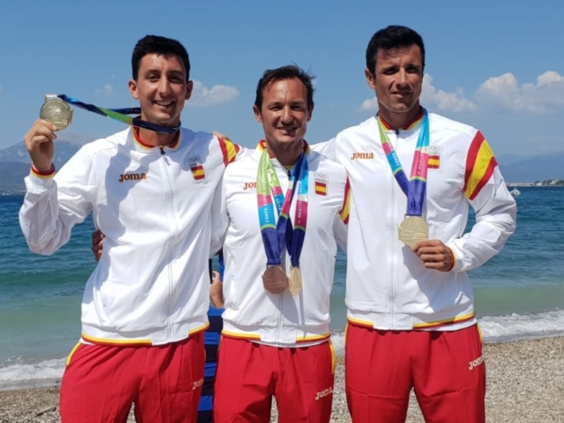 Tres atletas españoles celebran con medallas de oro en la playa.