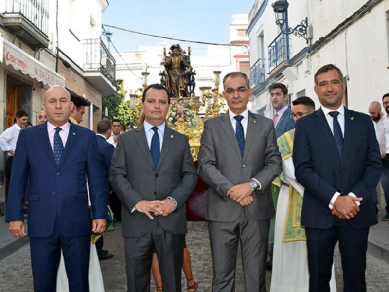 Oficiales y sacerdotes participan en una procesión religiosa en una calle de pueblo.