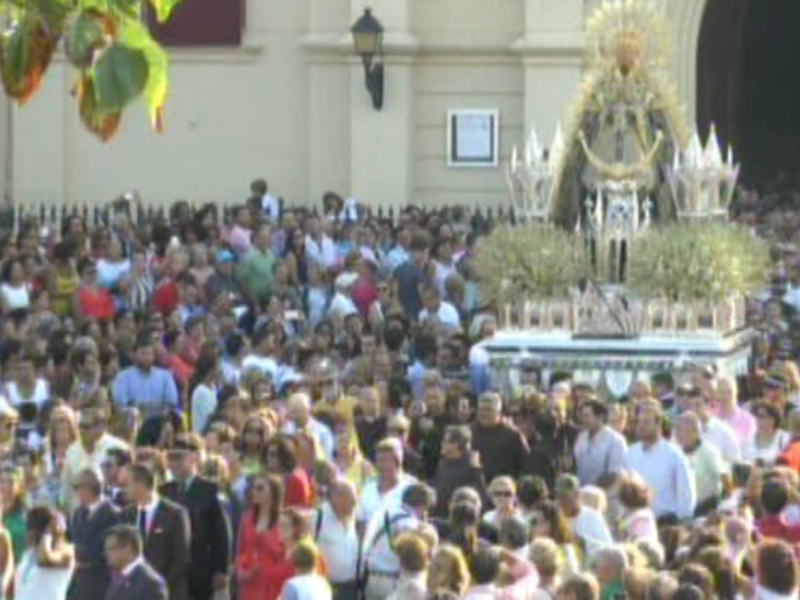 Una multitud de personas participa en una procesión religiosa, con una imagen de la Virgen en el centro. La imagen destaca por su majestuosidad y el ambiente festivo.