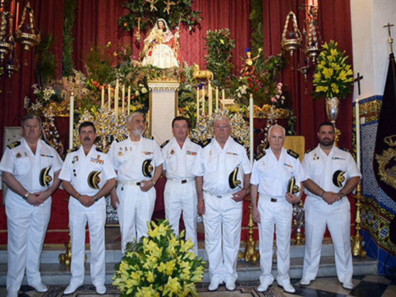 Oficiales en uniforme blanco posando frente a un altar con decoración floral y religiosa.