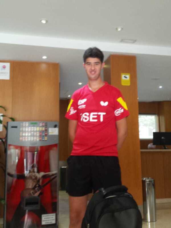 Persona en uniforme deportivo rojo en un lobby con maleta y máquina expendedora de bebidas.