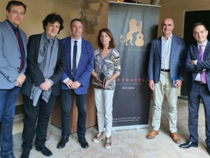 Grupo de personas posando frente a un cartel con la imagen de un león y una guitarra, en un entorno interior con paredes de piedra.