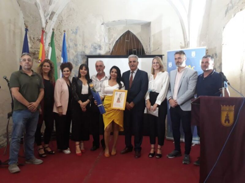 Celebración de un evento en un edificio histórico con una mujer sosteniendo un trofeo y un grupo de personas alrededor.