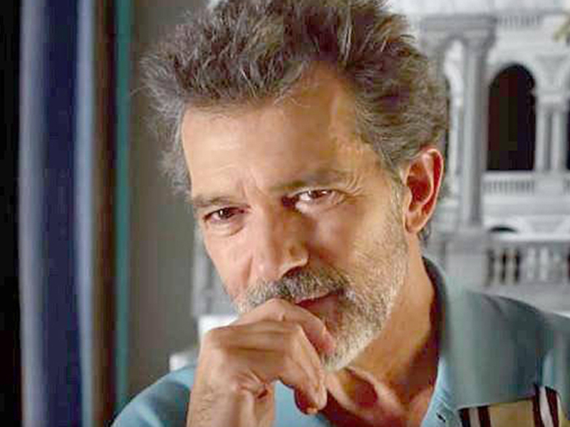 Un hombre con una barba gris y una camisa azul, con un edificio en el fondo.