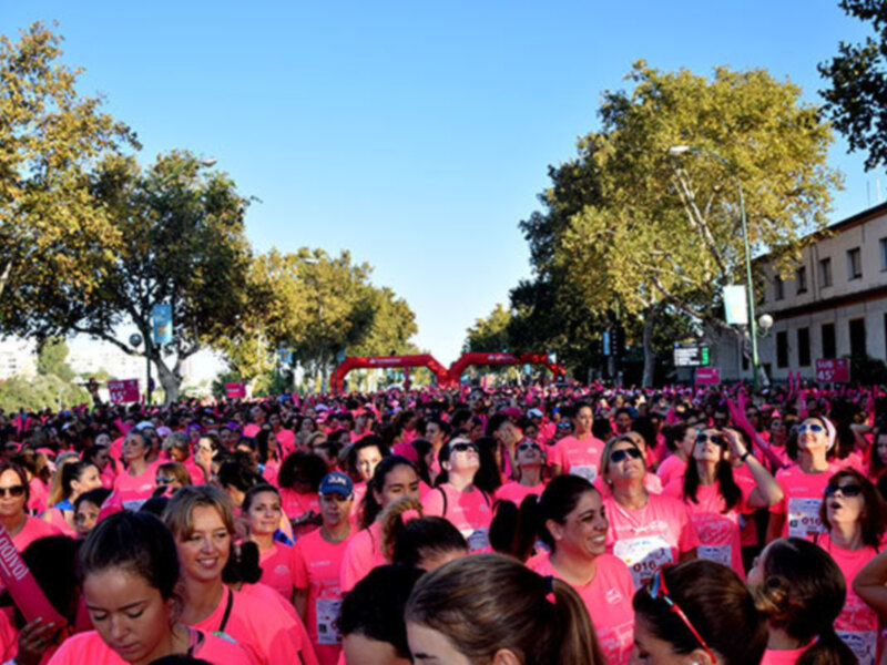 Marcha solidaria contra el cáncer de mama con participantes en camisetas rosas en una calle arbolada.