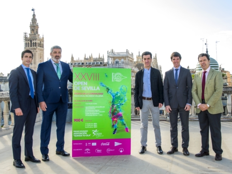 Cuatro hombres en trajes posan frente a un cartel promocional del Open de Sevilla, con la Giralda en el fondo.