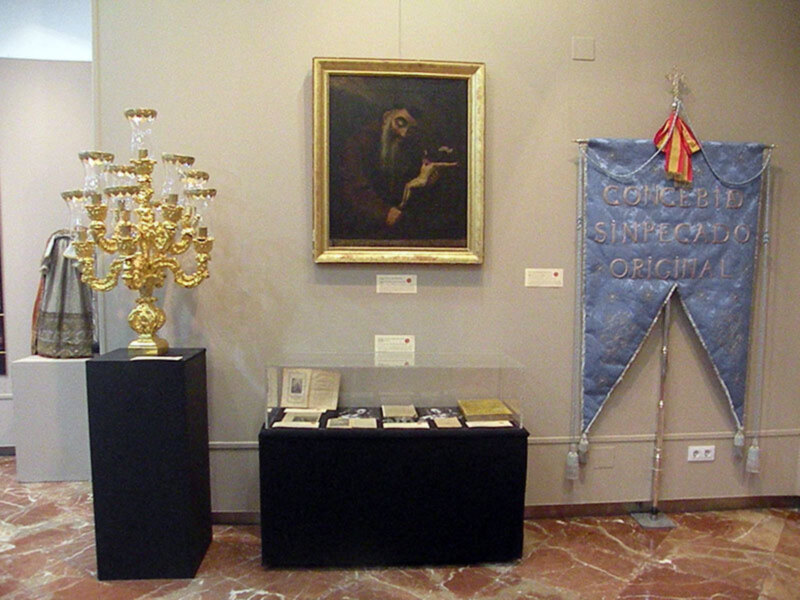 Exposición con artefactos históricos, un retrato enmarcado, un candelabro dorado y una bandera con texto en español.