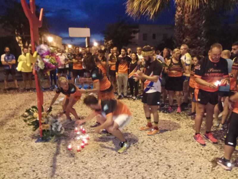 Un grupo de corredores se reúne en un acto de homenaje, encendiendo velas alrededor de un altar con flores y velas.